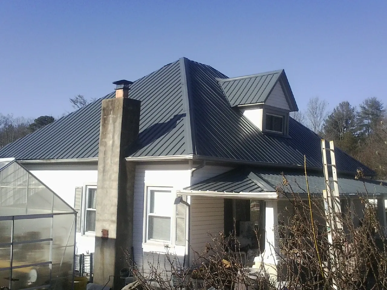 Dark blue standing seam metal roof on a white farmhouse with dormer — Slate & Tile Roof Repair by Roofing Brothers in Lindenhurst