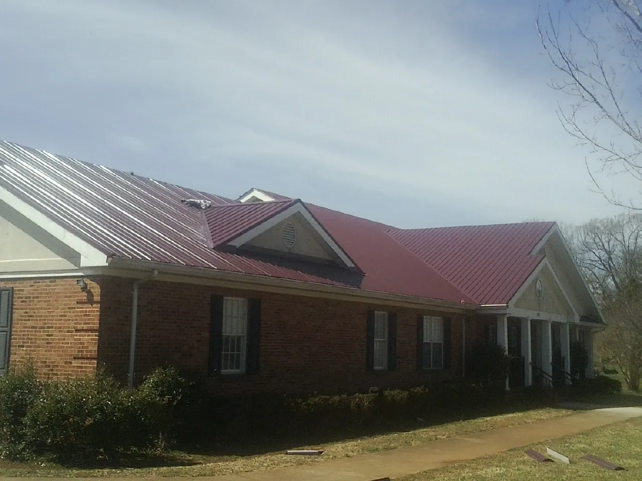 Red metal roof with gabled entries on a long brick building, from a Hail Damage Roof Repair job in Lindenhurst