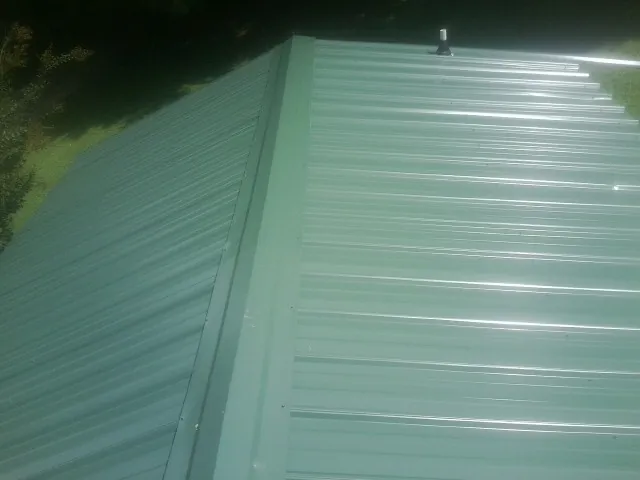 New green metal panels meeting at the ridge of a roof — Flat Roof Repair work by our crew in Lindenhurst