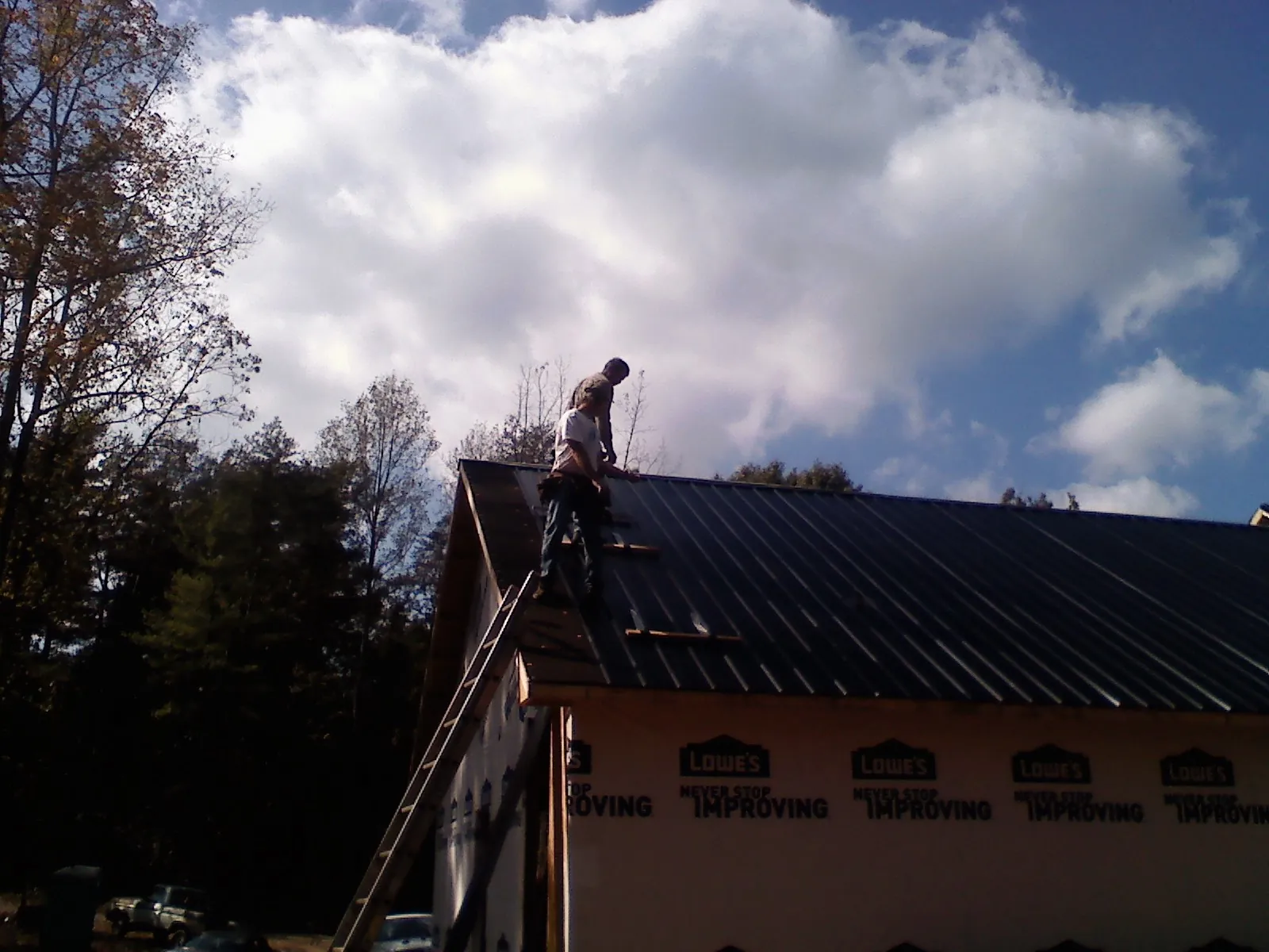 Roofer fastening dark metal panels high against a cloudy sky, from a Roof Inspection job in Lindenhurst