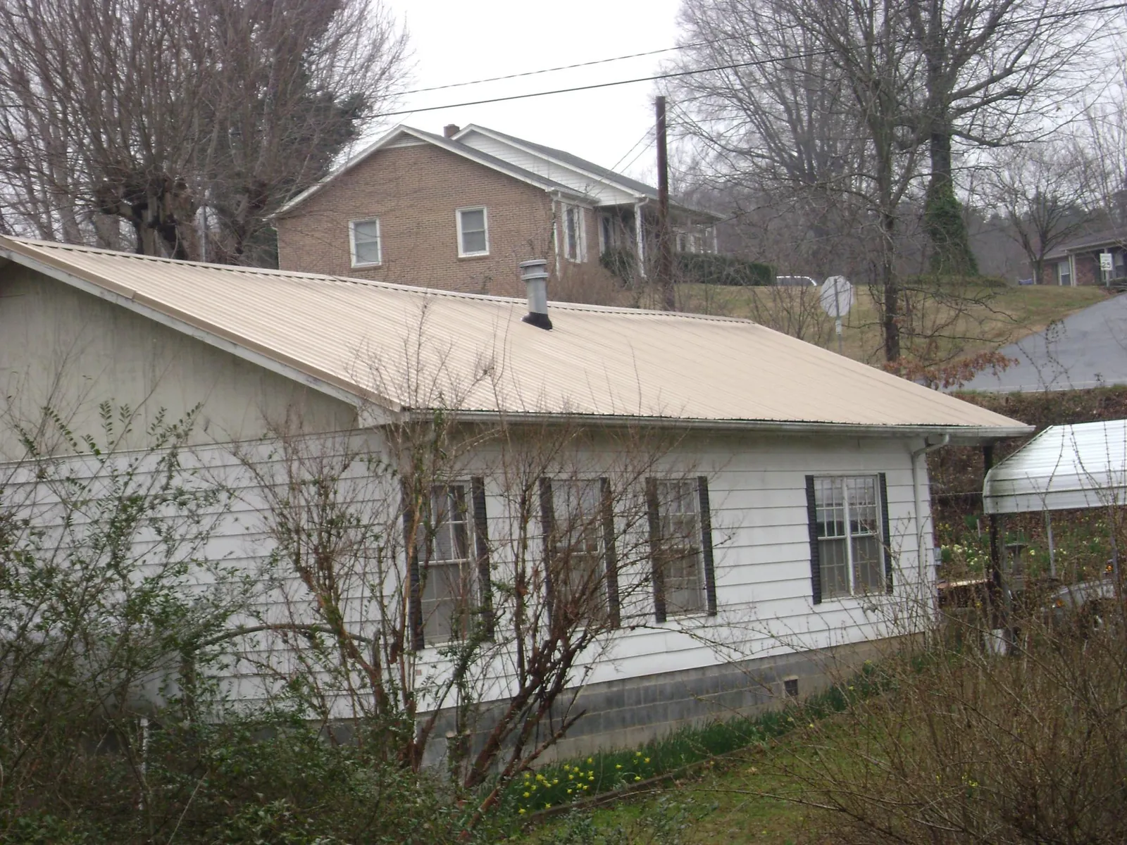 Tan metal roof on a white sided house set into a hillside — Commercial Roofing by Roofing Brothers in Lindenhurst